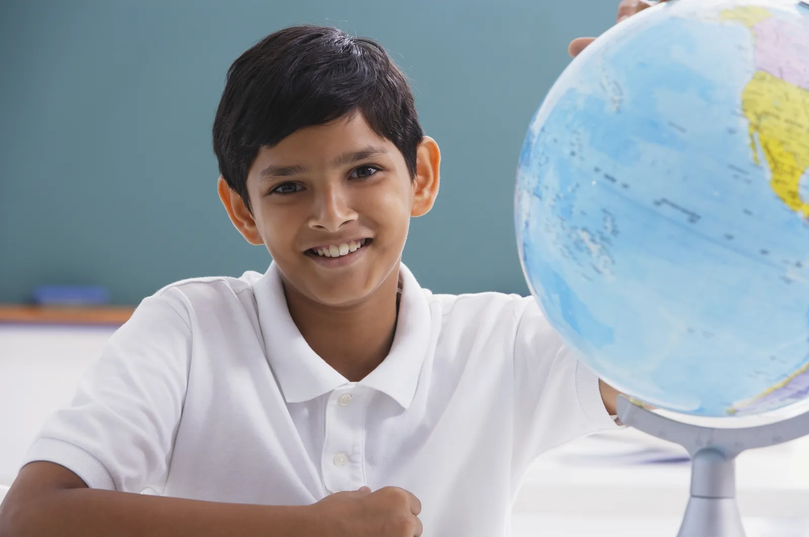A schoolboy holds a globe in a classroom