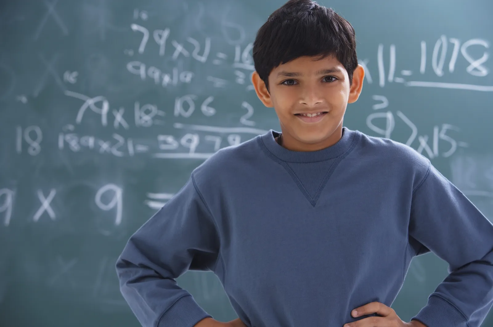 A schoolboy writes a maths problem on a classroom chalkboard