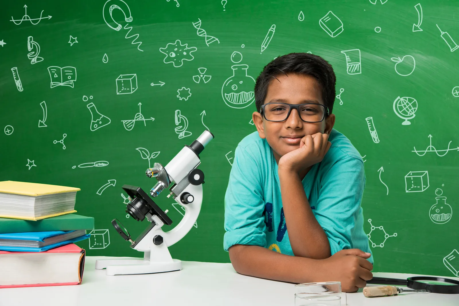 A schoolboy looks through a microscope beside a classroom chalkboard